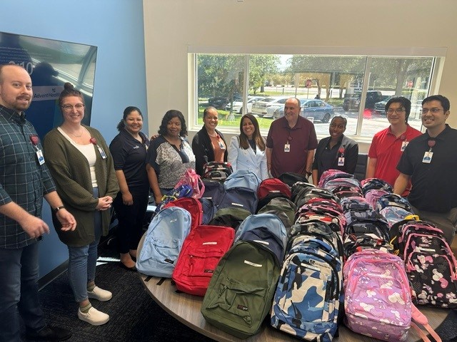 employees gather around table with backpacks for donation